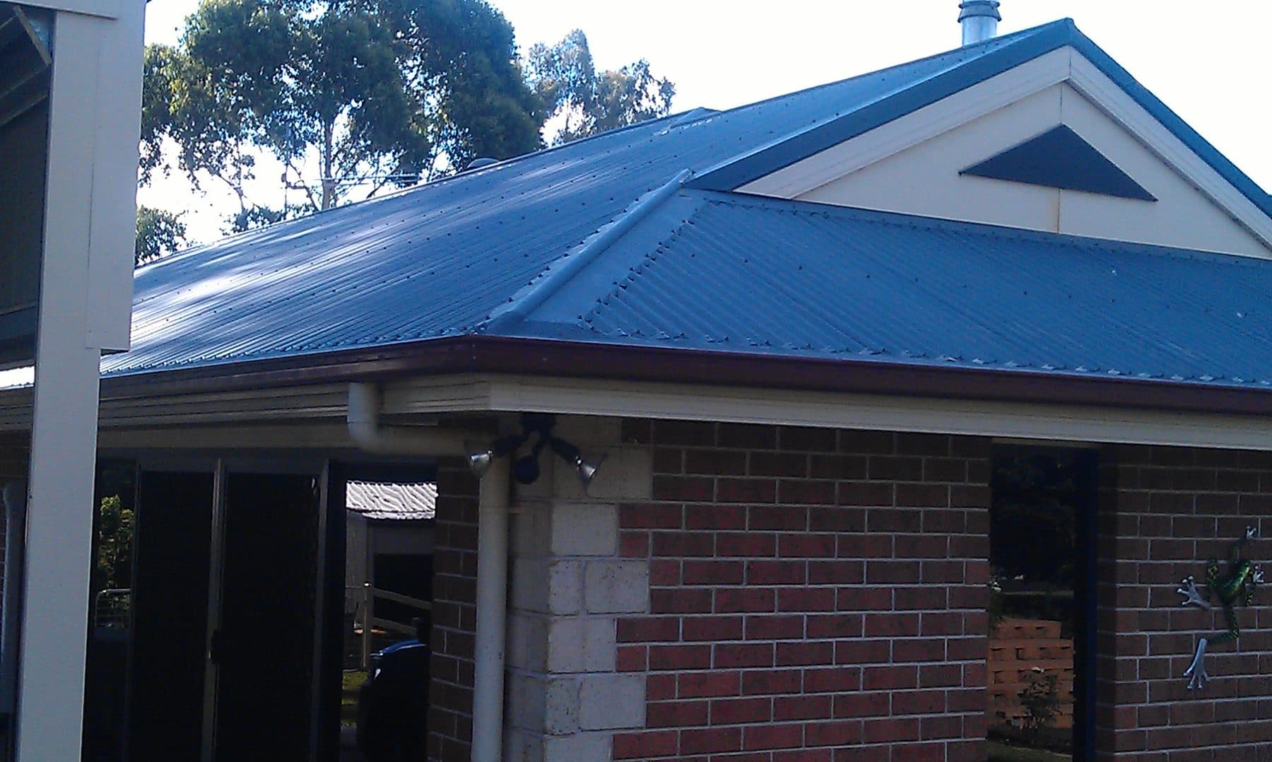 A brick home with a blue metal roof and gutter guard along the eaves