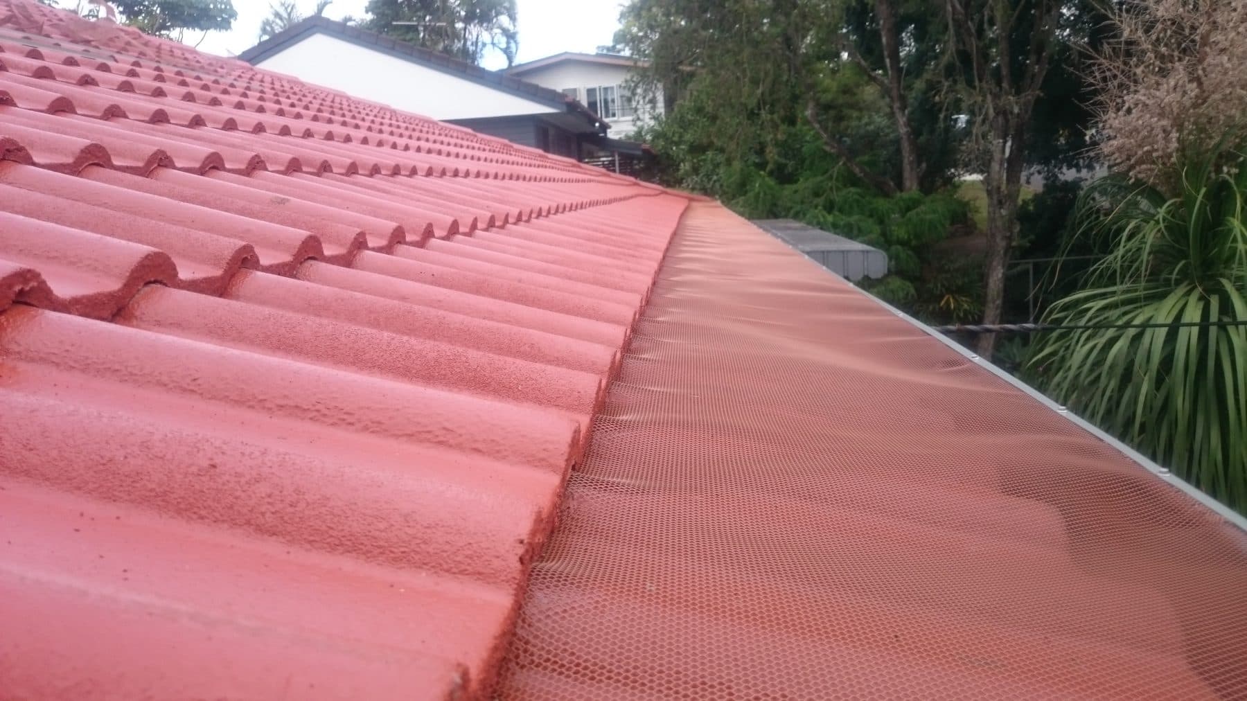 Gutter guard on a red tile roof above a suburban street